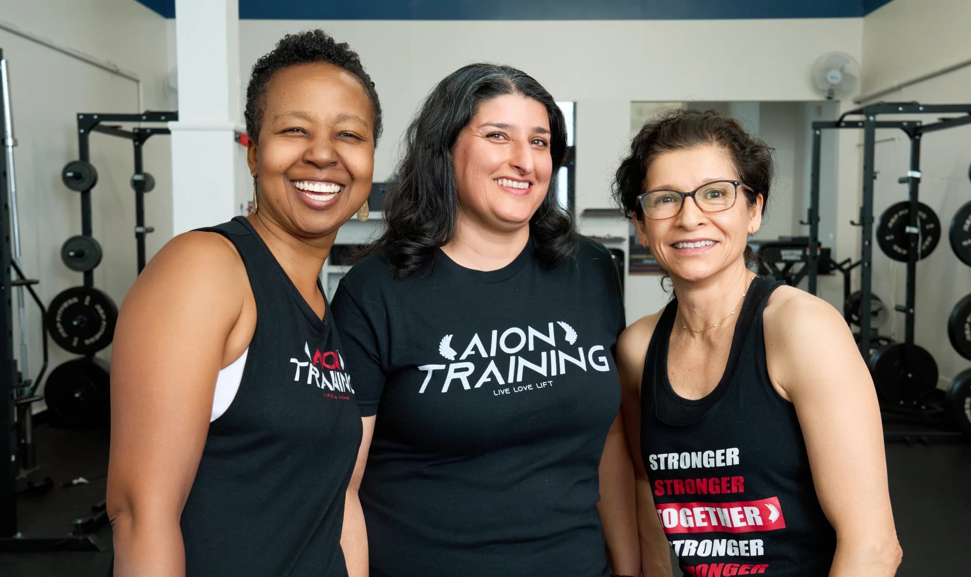 Three members in Aion shirts stand together smiling in the studio.